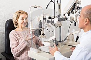 Mature optician examinating eyesight with aid of slit lamp