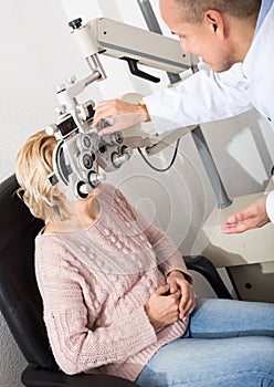 Mature optician examinating eyesight with aid of slit lamp