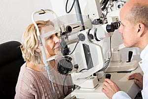 Mature optician examinating eyesight with aid of slit lamp