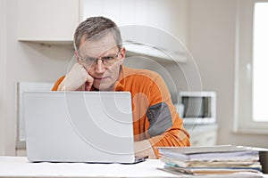 Mature pensive man working remote from home with laptop and files