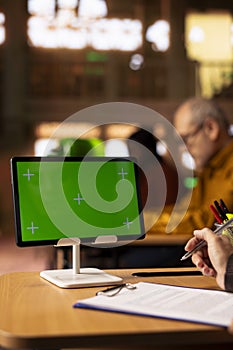 Mature person working on her thesis next to green screen display at the library