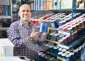 Mature positive man selecting wall paint and emulsion in store