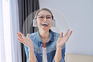 Mature positive talking middle aged woman in headphones looking at camera