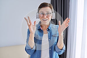 Mature positive talking middle aged woman in headphones looking at camera