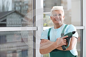 Mature repairman with electric screwdriver near plastic window indoors. Space for text