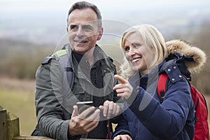 Mature Retired Couple Walk In Fall Or Winter Countryside Using Map Or Navigation App On Mobile Phone