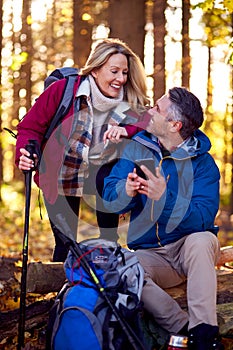 Mature Retired Couple Walk In Fall Or Winter Countryside Using Map Or Navigation App On Mobile Phone