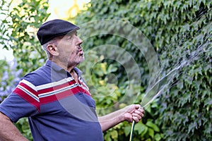 Mature retired man whistles while watering his green garden at home
