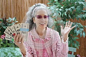 Mature rich smiling woman holding bundles of dollars