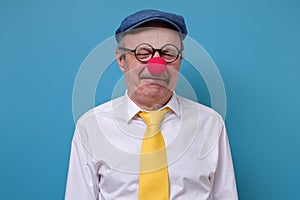 Mature sad stressed man wearing clown nose isolated on blue background