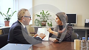 Mature salesman and senior woman discussing mortgage contract in office of real estate agency.