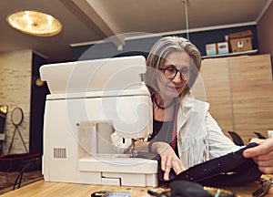 Mature seamstress works, sews clothes on sewing machine. Process of tailoring and repair of clothing in an atelier or workshop.