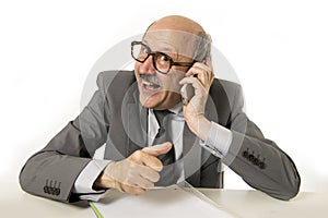 Mature senior business man talking on mobile phone at office desk working happy and gesturing funny