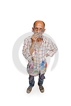 Mature or senior grey painter with a brush standing in front of camera. Funny man in a paint-stained shirt fooling