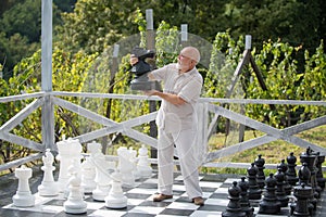 Mature senior playing chess on big chessboard in the park. Chess game for old man. Older grandfather, grandpa pensioner