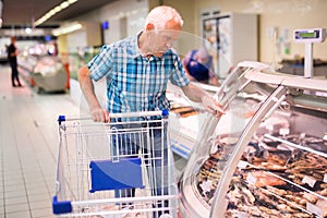 mature senor choosing dried fish in supermarket photo