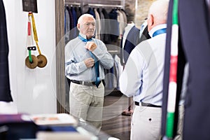 Mature shopper tries on fashionable tie in front of mirror in clothing store
