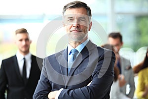 Mature smiling business manager crossing his arms in front of his business team.