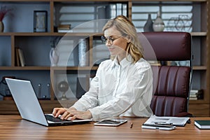 Mature smiling businesswoman working in evening inside home office, woman using laptop at work, typing on keyboard