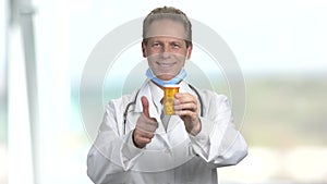 Mature smiling doctor offers can of pills.