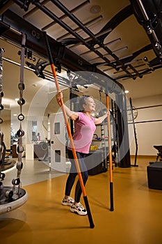 Mature smiling european woman doing sport exercise with sports sticks in gym