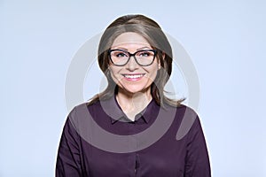 Mature smiling woman in glasses looking at camera on light background