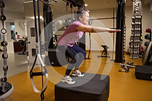 Mature smiling woman wearing sportswear doing sport exercise on sport box in gym