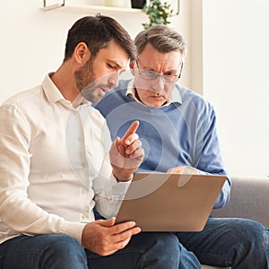 Mature Son Explaining Father How To Use Laptop Sitting Indor