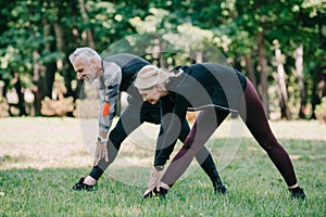 Mature sportsman and sportswoman stretching in park together