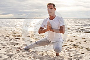 Mature sporty man practicing yoga in beach