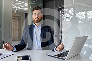 Mature successful senior experienced man meditating in lotus position inside office, businessman with closed eyes