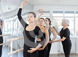 Mature teacher conducts class with girls in ballet studio, observes doing forth position exercise.