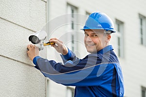 Mature Technician Installing Camera On Wall With Screwdriver