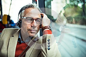 Mature tired businessman with heaphones travelling by bus in city.