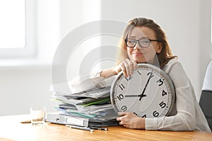 Mature tired woman with clock at table in office. Time management concept