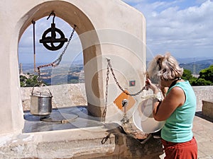 Mature tourist woman drinks fresh water from old draw well