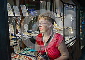 Mature tourist woman looks at showcase of golden jewellery shop