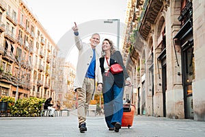 Mature tourists pointing and walking with a suitcase on vacations. Middle aged couple having fun sightseeing on a