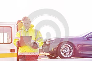 Mature tow truck driver making reports on clipboard against sky