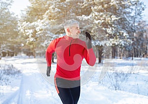 Mature trail runner training for marathon in beautiful snowy forest. Outdoor seasonal sports concept