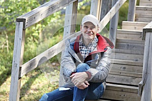 Mature traveler resting on wooden stairs of a tourist footpath outdoors