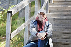 Mature traveler resting on wooden stairs of a tourist footpath outdoors