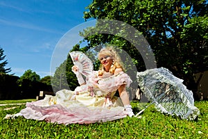 Mature vintage woman in Venetian costume lying on the green park with white umbrella