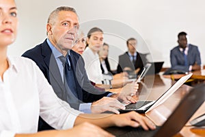 Mature white businessman sitting at meeting and listening to presentation