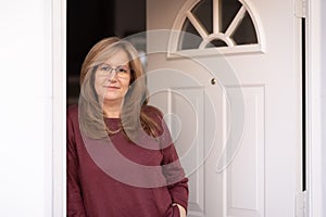 Mature white woman at the door of her house in a happy attitude