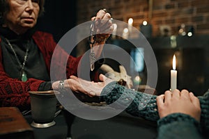 Mature witch using crystal pendulum to predict future for client