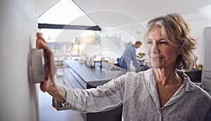 Mature Woman Adjusting Wall Mounted Digital Central Heating Thermostat Control At Home