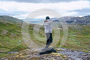 Mature woman adjusts warmer clothes, hiking at high altitude cold Norwegian Mountains range terrain. Hiking high in Norwegian