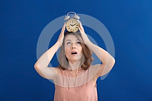 Mature woman with alarm clock on head against color background. Time management concept