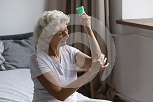 Mature woman apply nourishing body cream on arms
